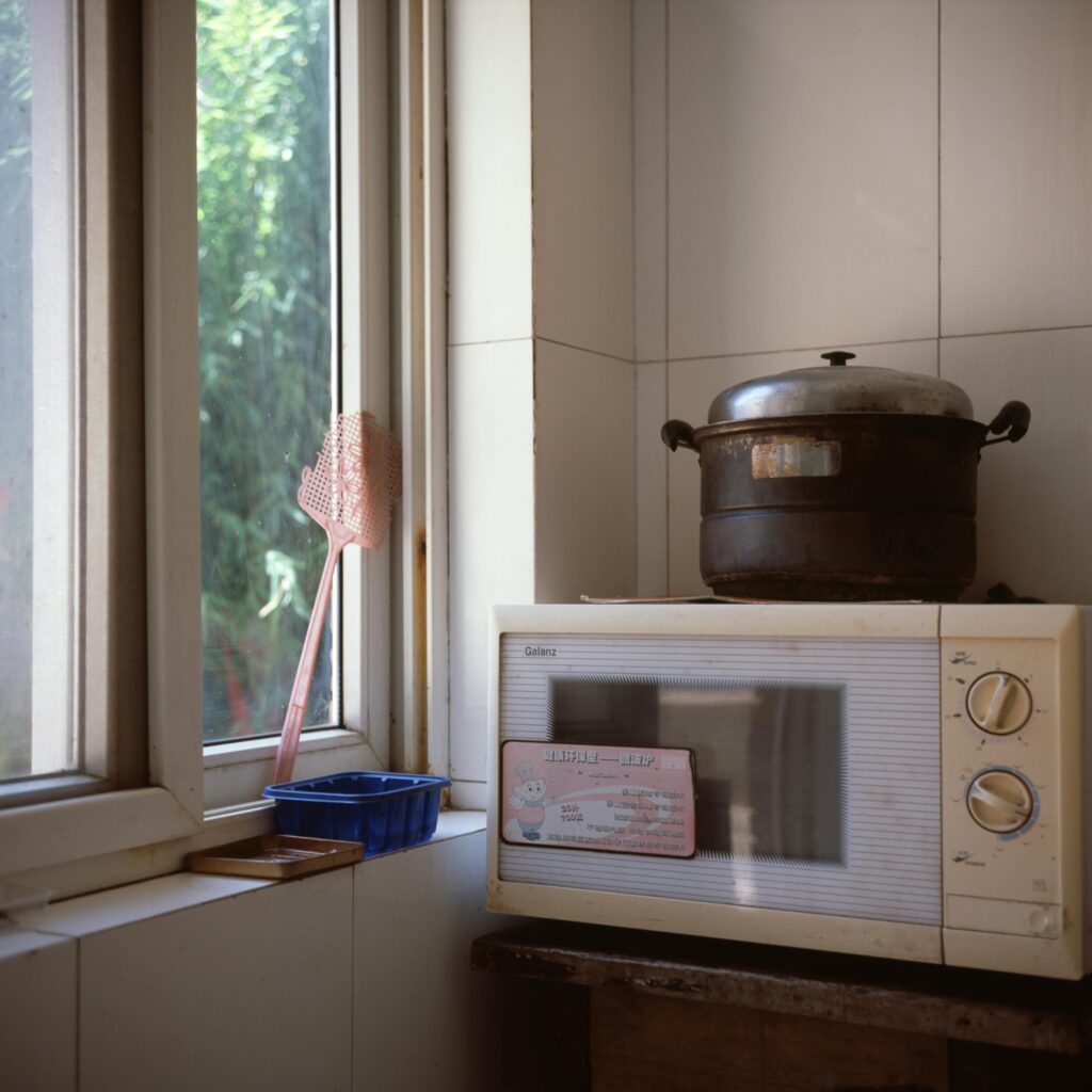 Sunlit kitchen corner with a microwave, vintage pot, and window view.
